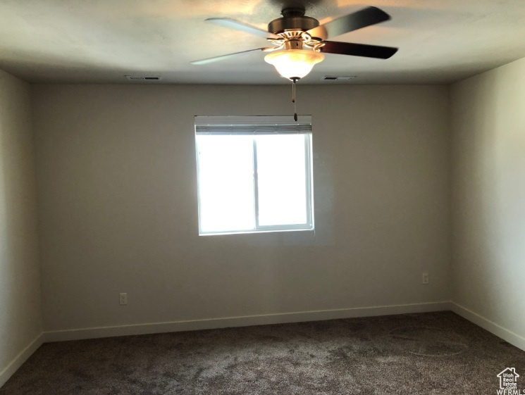 Spare room with baseboards, a ceiling fan, dark carpet, and visible vents