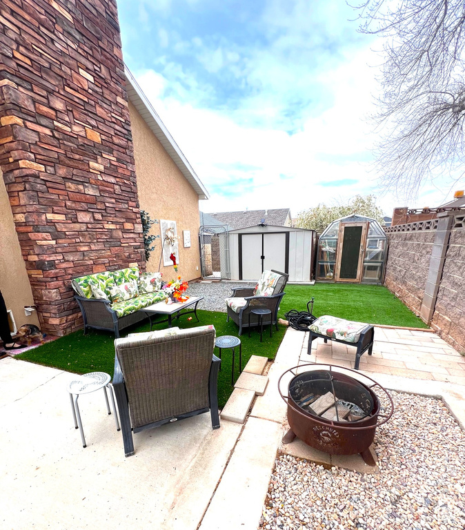 View of patio featuring a fenced backyard, a storage unit, an outbuilding, and an outdoor living space with a fire pit