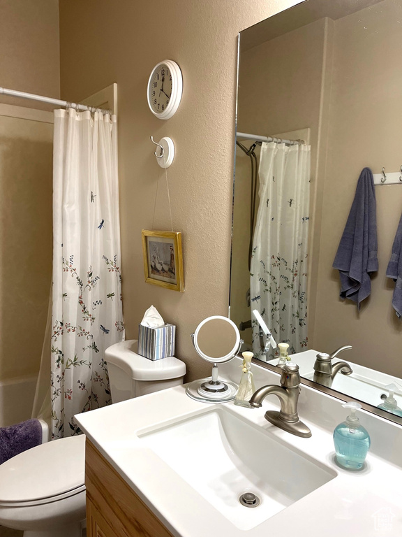 Full bathroom featuring toilet, a textured wall, shower / bath combo with shower curtain, and vanity