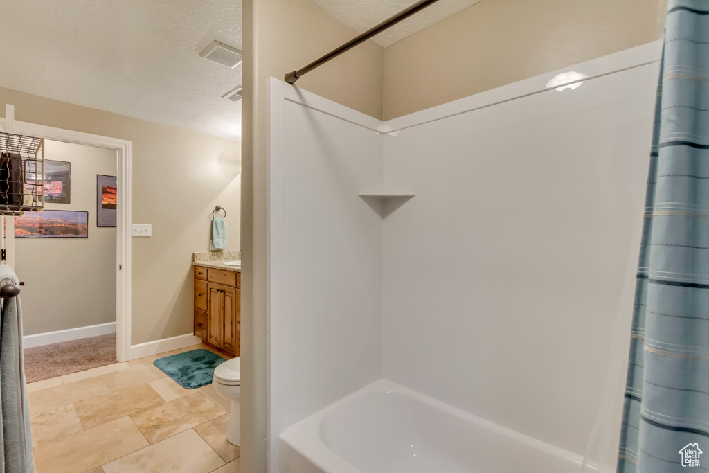 Bathroom with a textured ceiling, toilet, baseboards, shower / tub combo, and vanity