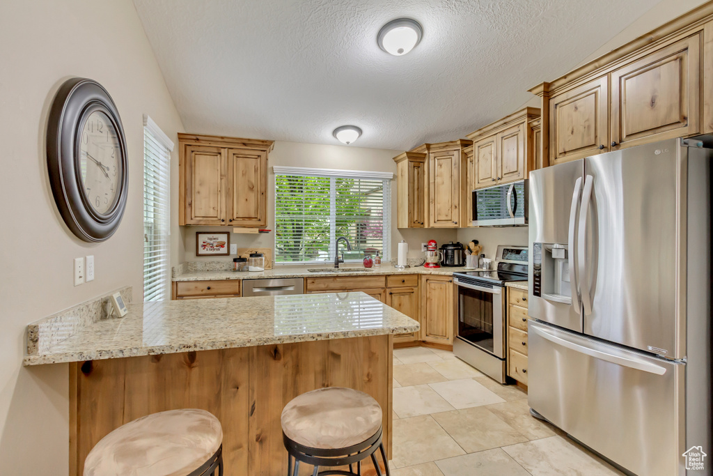 Kitchen featuring a peninsula, a sink, a textured ceiling, a breakfast bar, and appliances with stainless steel finishes