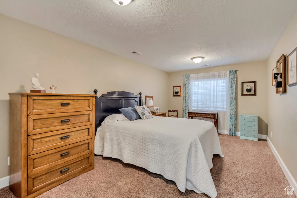 Bedroom with light carpet, a textured ceiling, visible vents, and baseboards