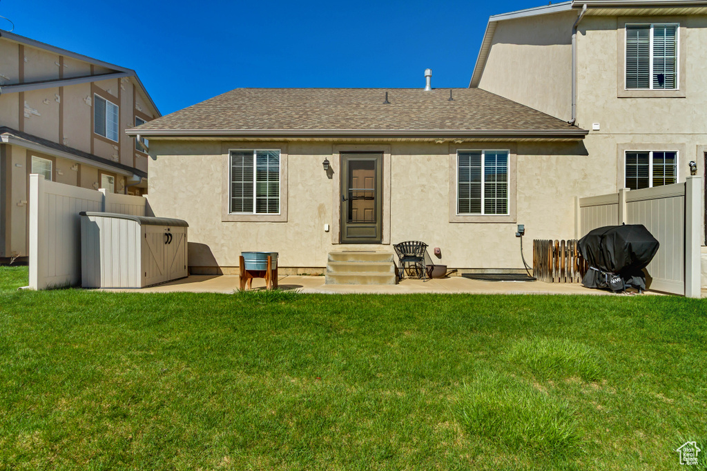 Rear view of property featuring roof with shingles, fence, entry steps, a yard, and stucco siding