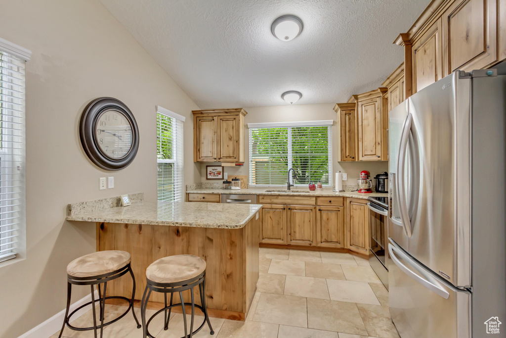 Kitchen with light stone counters, a sink, a breakfast bar area, a peninsula, and appliances with stainless steel finishes