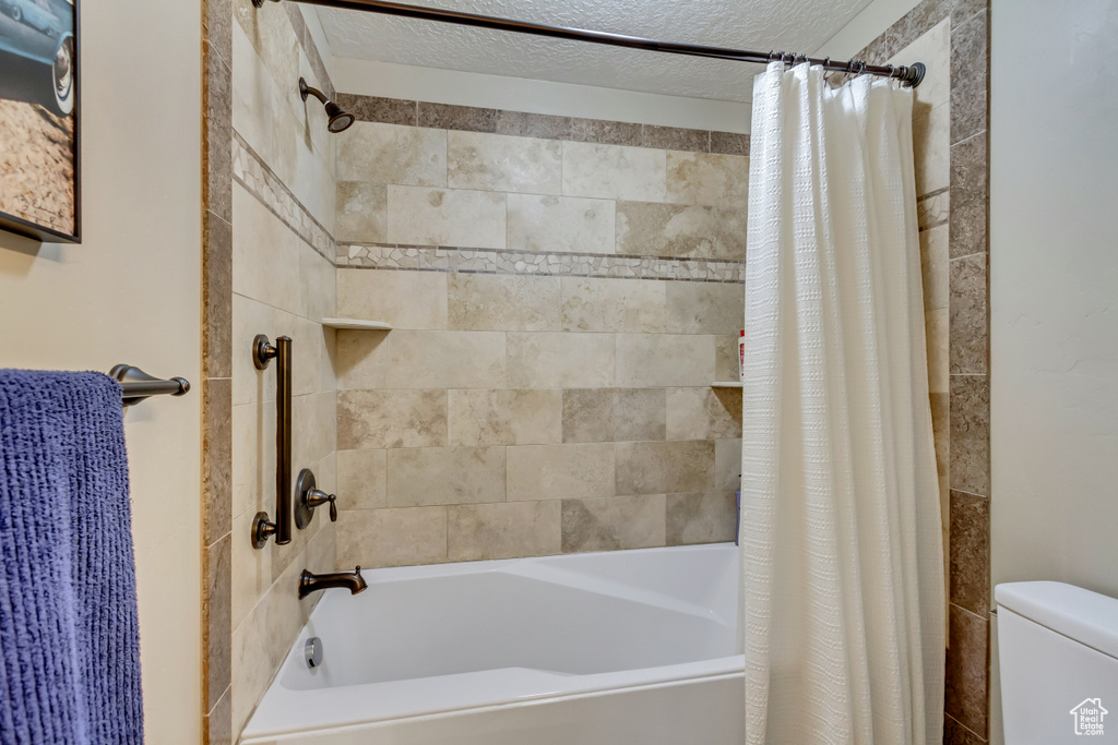Full bathroom featuring toilet, shower / tub combo with curtain, and a textured ceiling