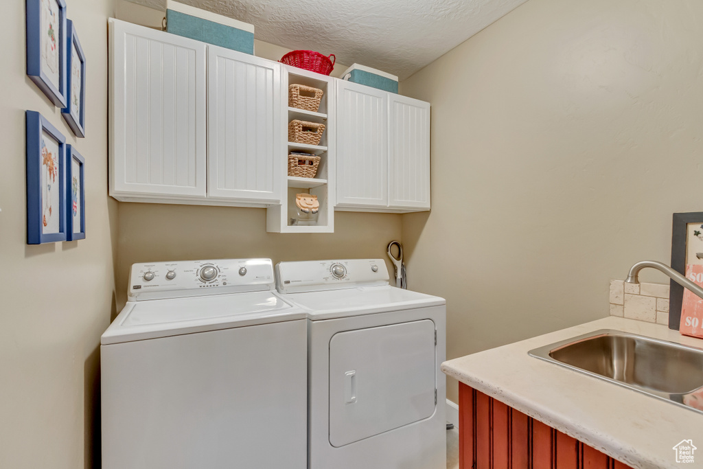 Clothes washing area featuring washing machine and clothes dryer, a sink, a textured ceiling, and cabinet space