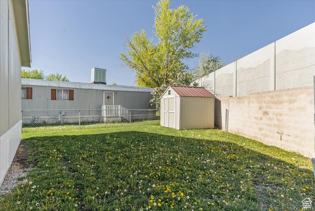 View of yard featuring a storage unit, a fenced backyard, central AC, and an outdoor structure