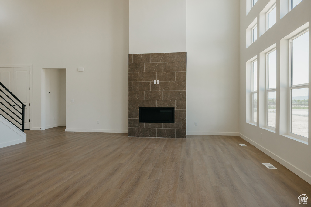 Unfurnished living room featuring a towering ceiling, light wood-style floors, stairway, a glass covered fireplace, and baseboards