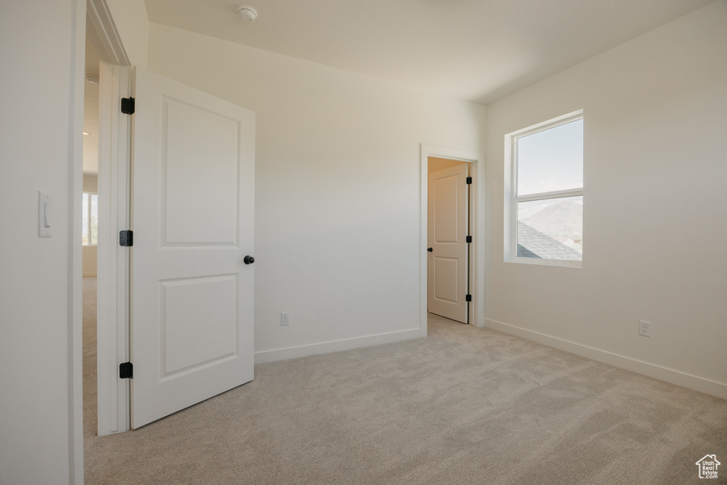 Unfurnished bedroom with light colored carpet and baseboards