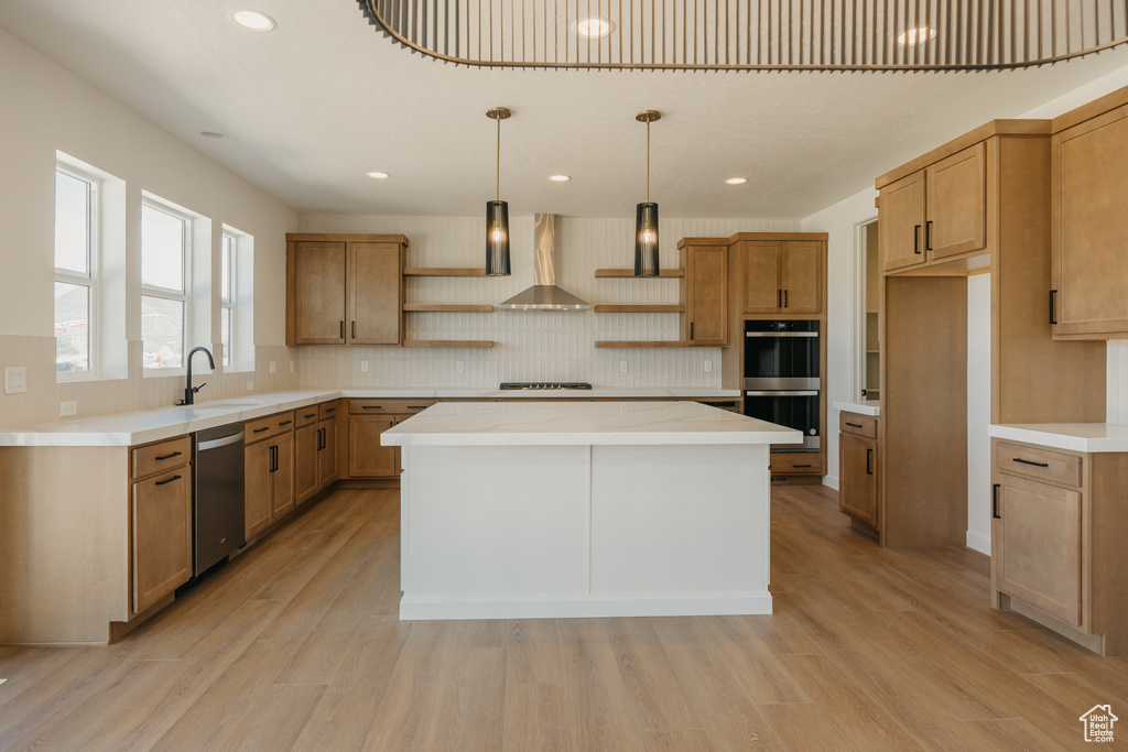 Kitchen featuring dishwasher, open shelves, multiple ovens, wall chimney exhaust hood, and light wood-type flooring