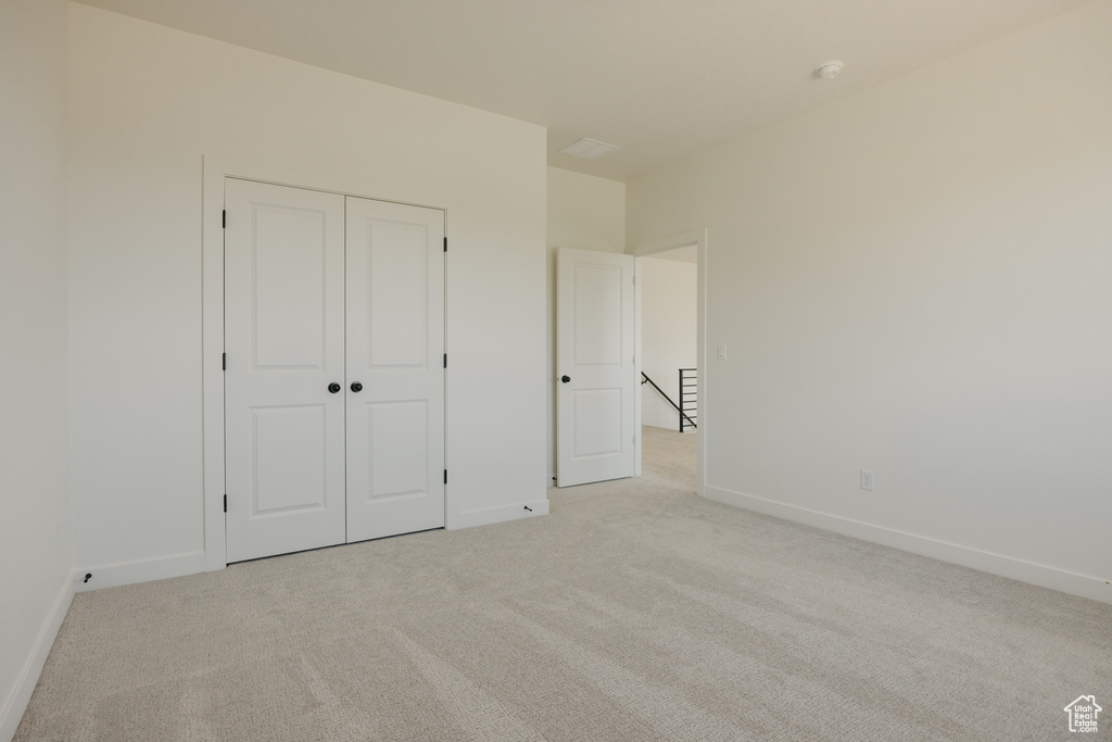 Unfurnished bedroom featuring light carpet, baseboards, and a closet