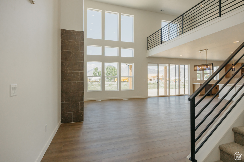 Unfurnished living room with stairway, wood finished floors, plenty of natural light, baseboards, and a high ceiling
