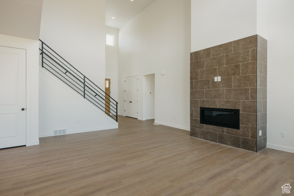 Unfurnished living room featuring light wood-style floors, stairs, a towering ceiling, baseboards, and a fireplace