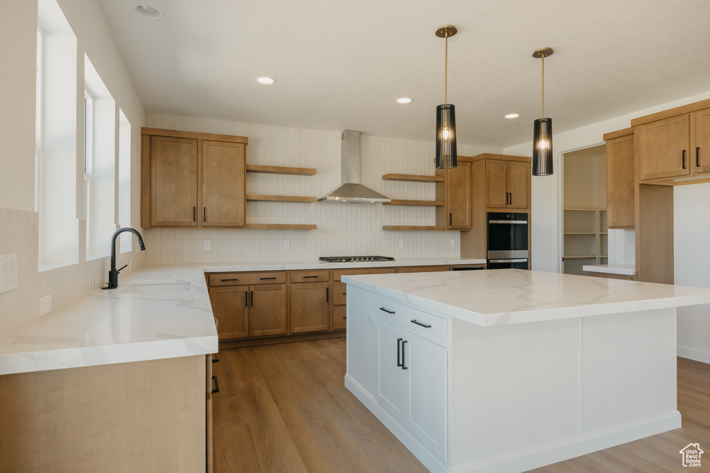 Kitchen featuring open shelves, wall chimney exhaust hood, a sink, a center island, and light wood-style floors