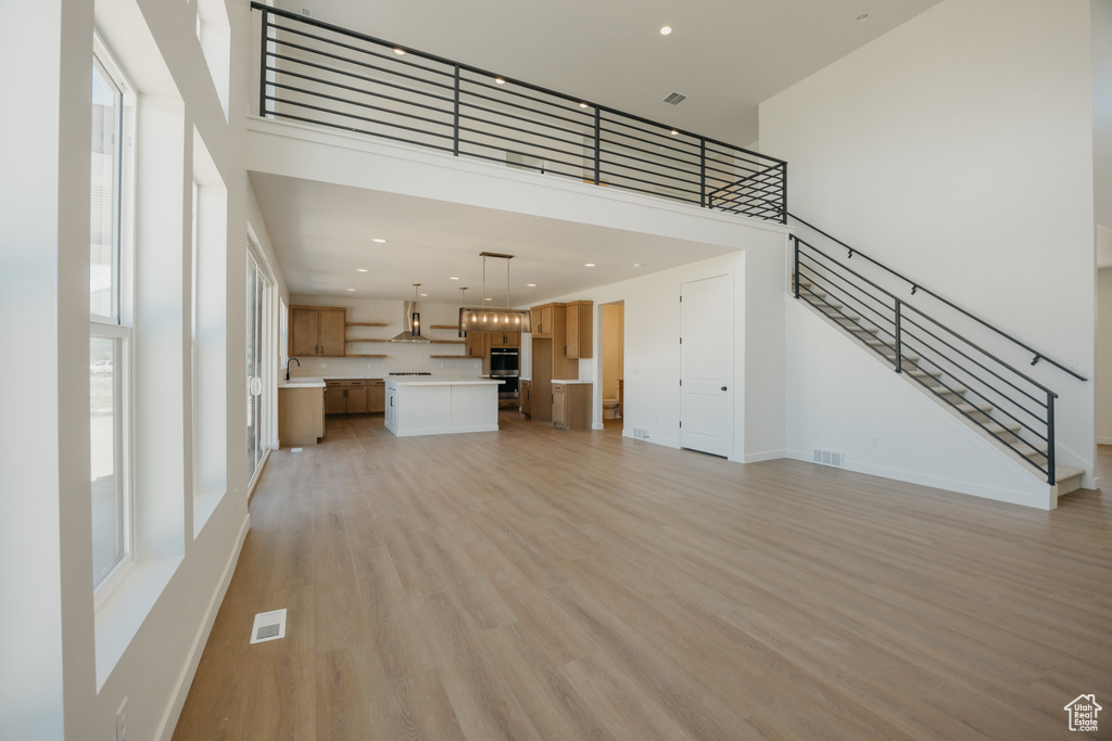 Unfurnished living room with a high ceiling, stairway, light wood-style flooring, baseboards, and recessed lighting