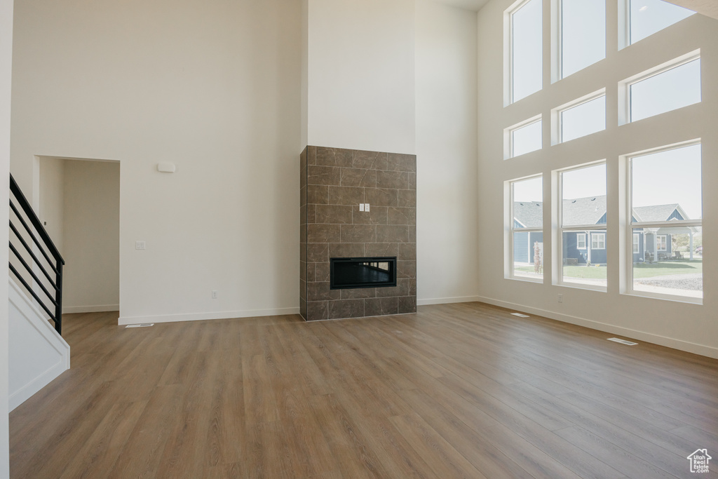 Unfurnished living room featuring a towering ceiling, light wood finished floors, baseboards, a tiled fireplace, and stairs