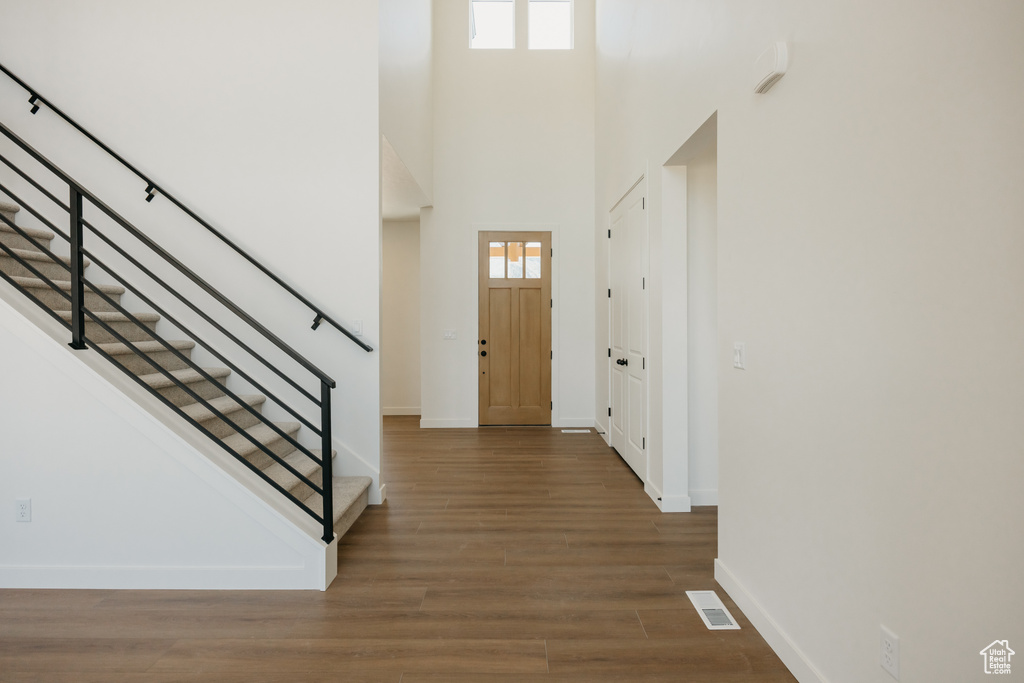 Foyer entrance with baseboards, wood finished floors, stairs, and a towering ceiling