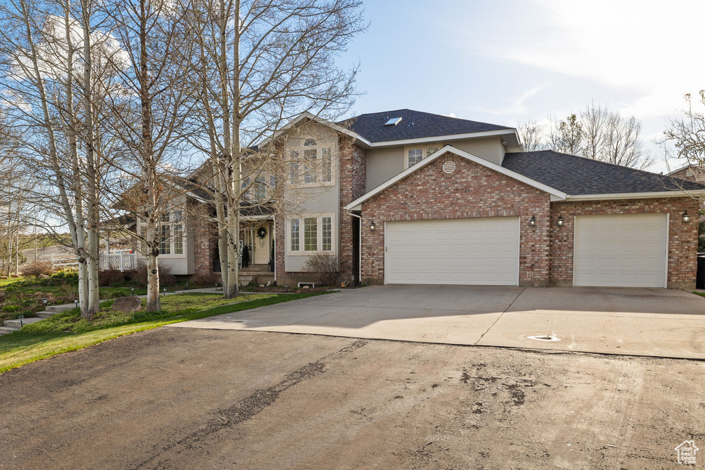 Traditional-style home with an attached garage, a shingled roof, driveway, and brick siding