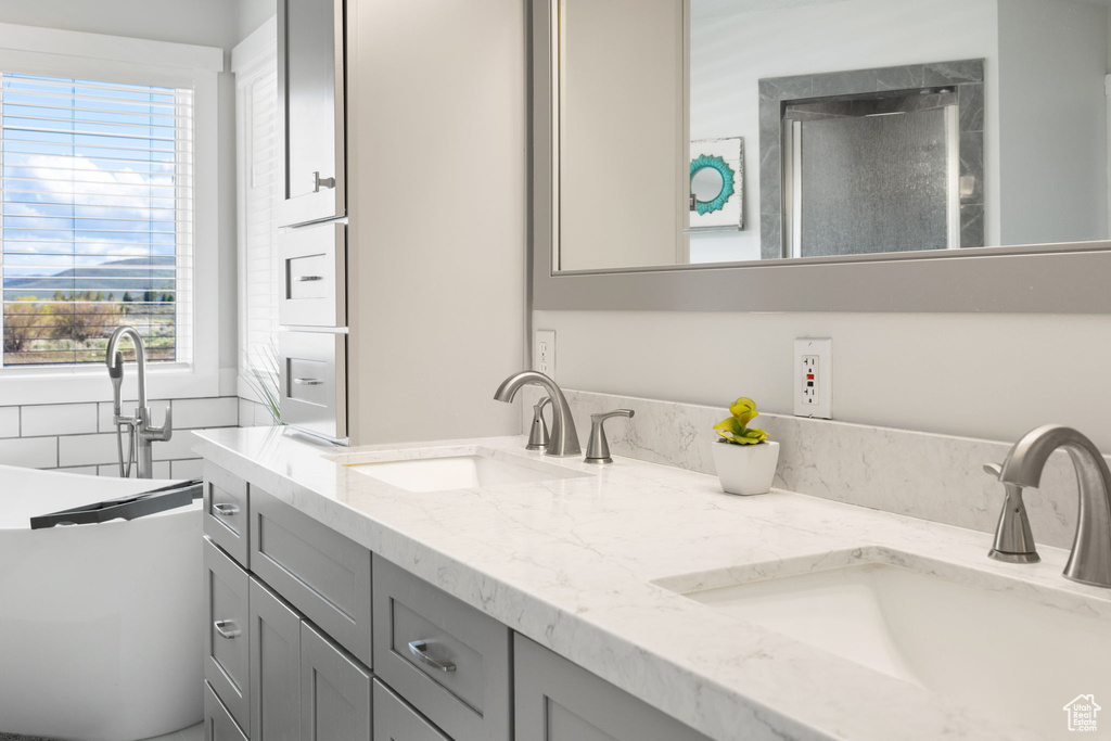 Full bath with double vanity, a sink, a shower with shower door, and a soaking tub