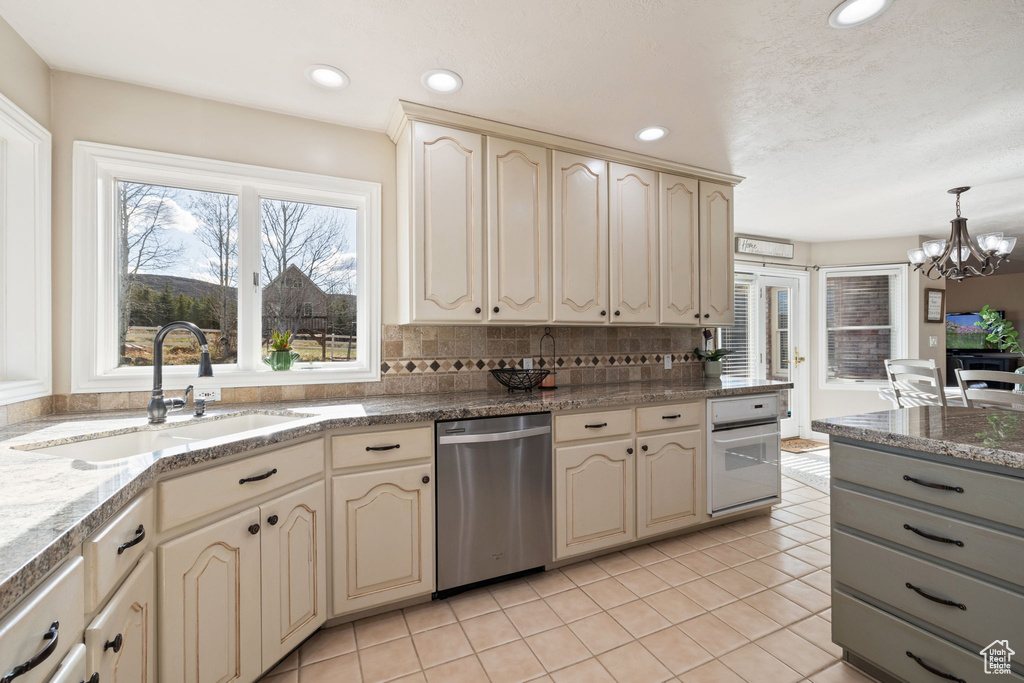 Kitchen with stainless steel dishwasher, a sink, light tile patterned floors, oven, and cream cabinetry