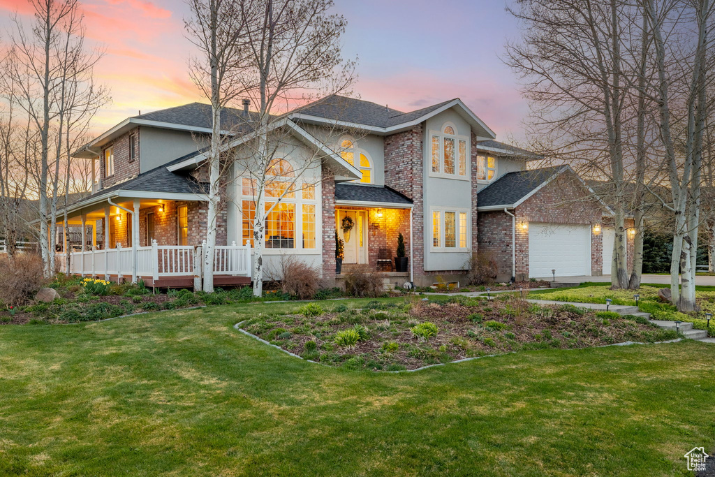 Traditional home with an attached garage, a yard, brick siding, and covered porch