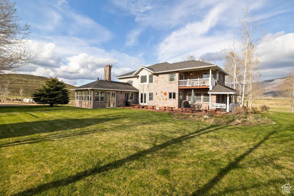 Rear view of house with a yard, brick siding, a chimney, and a balcony