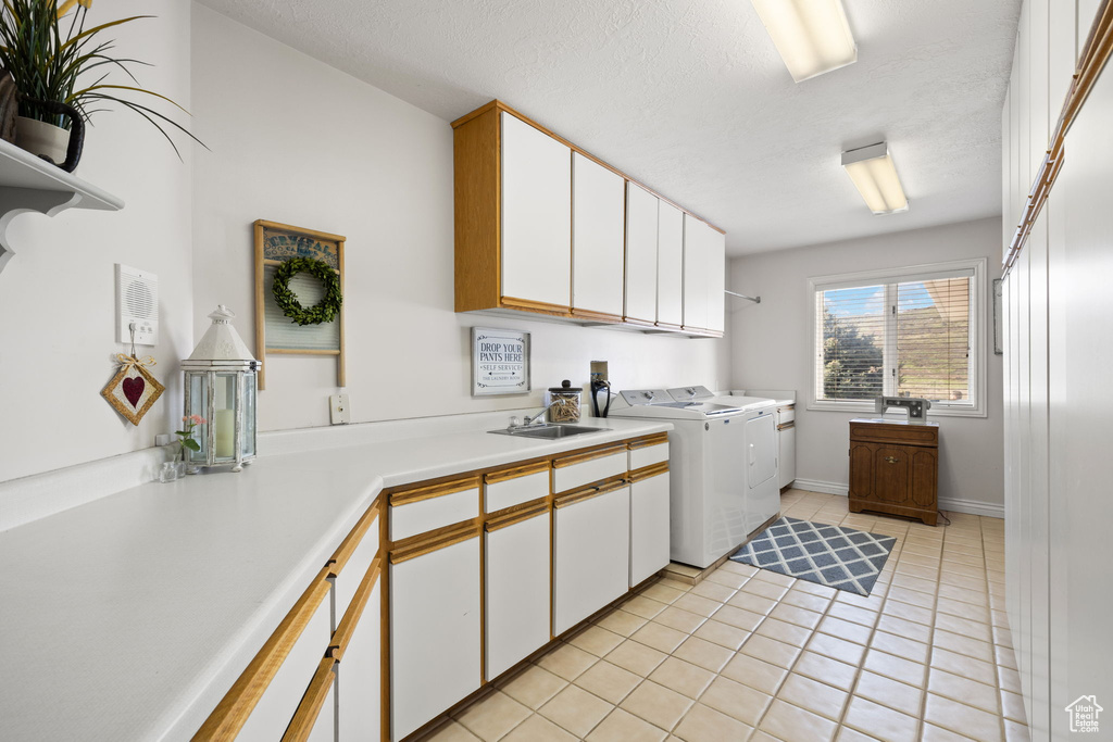 Laundry room featuring light tile patterned flooring, washer and clothes dryer, a textured ceiling, a sink, and cabinet space