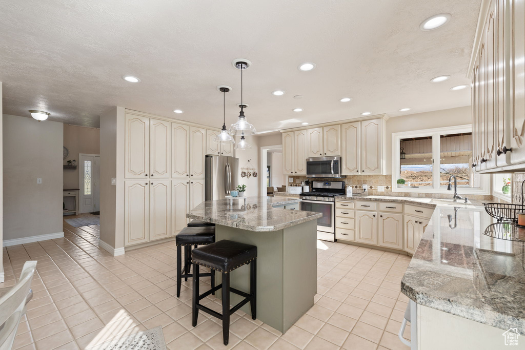 Kitchen featuring a kitchen bar, a sink, light tile patterned floors, stainless steel appliances, and recessed lighting