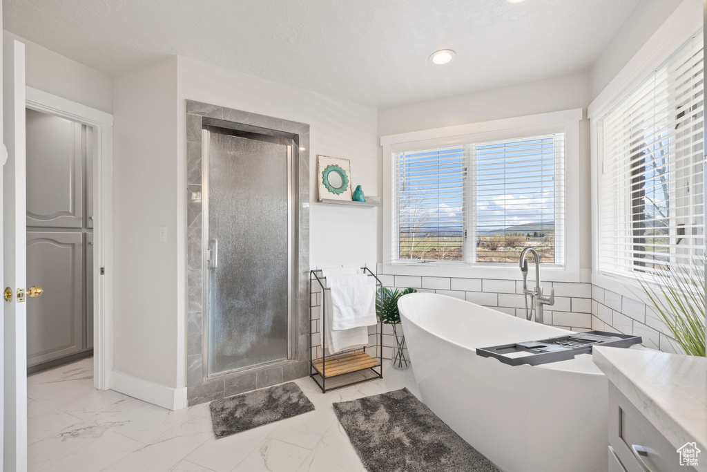 Bathroom featuring a freestanding tub, plenty of natural light, a stall shower, and marble finish floor