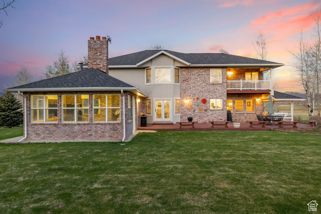 Back of property at dusk with a chimney, a lawn, brick siding, a balcony, and a patio