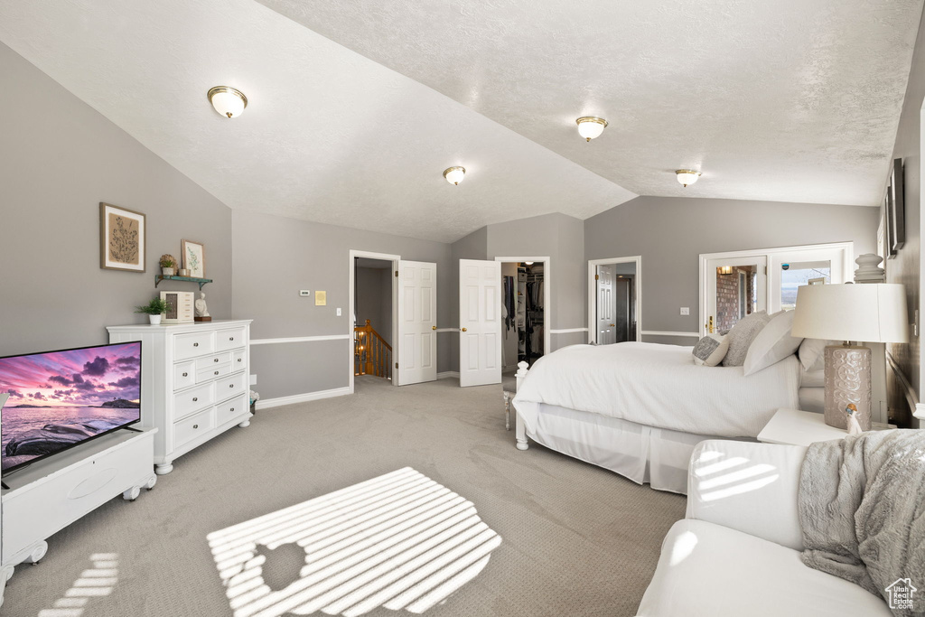Bedroom featuring a closet, light carpet, baseboards, a walk in closet, and vaulted ceiling