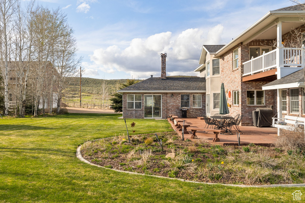Rear view of house with a deck, brick siding, a balcony, a yard, and a shingled roof