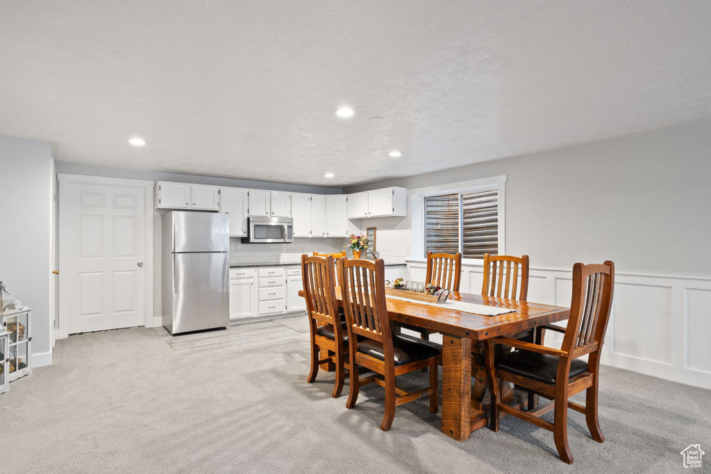 Dining area featuring a decorative wall, wainscoting, recessed lighting, and light colored carpet