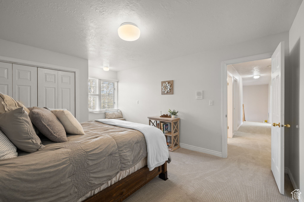 Bedroom with a textured ceiling, baseboards, light carpet, and a closet