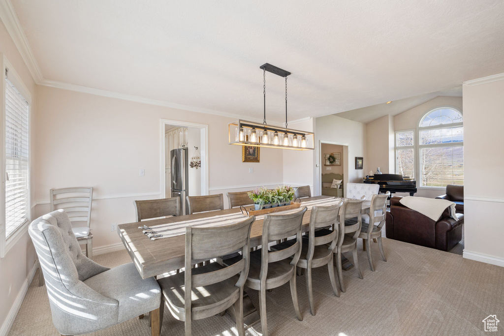 Dining space featuring crown molding, baseboards, light colored carpet, and lofted ceiling