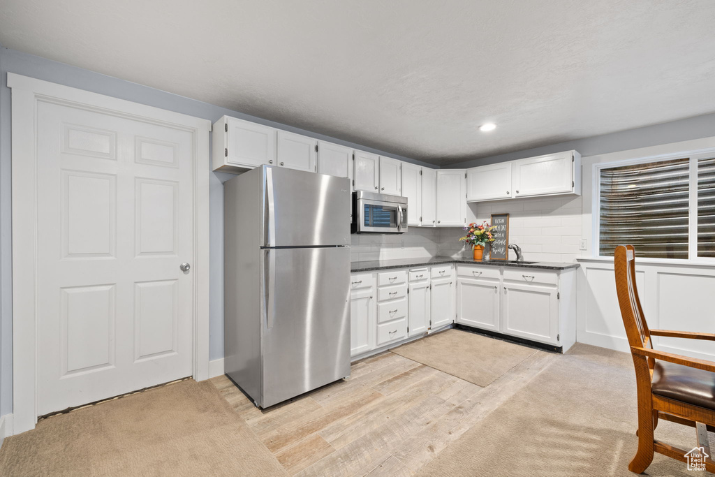 Kitchen with dark countertops, light wood-style flooring, stainless steel appliances, and white cabinetry