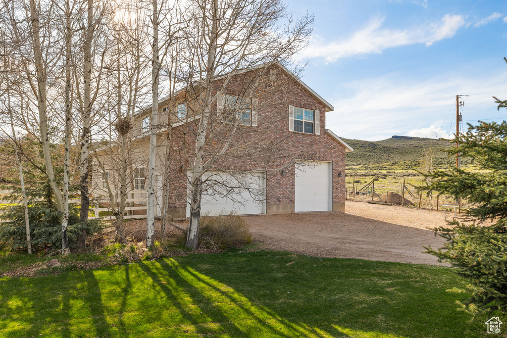 View of side of property featuring brick siding, dirt driveway, an attached garage, and a lawn