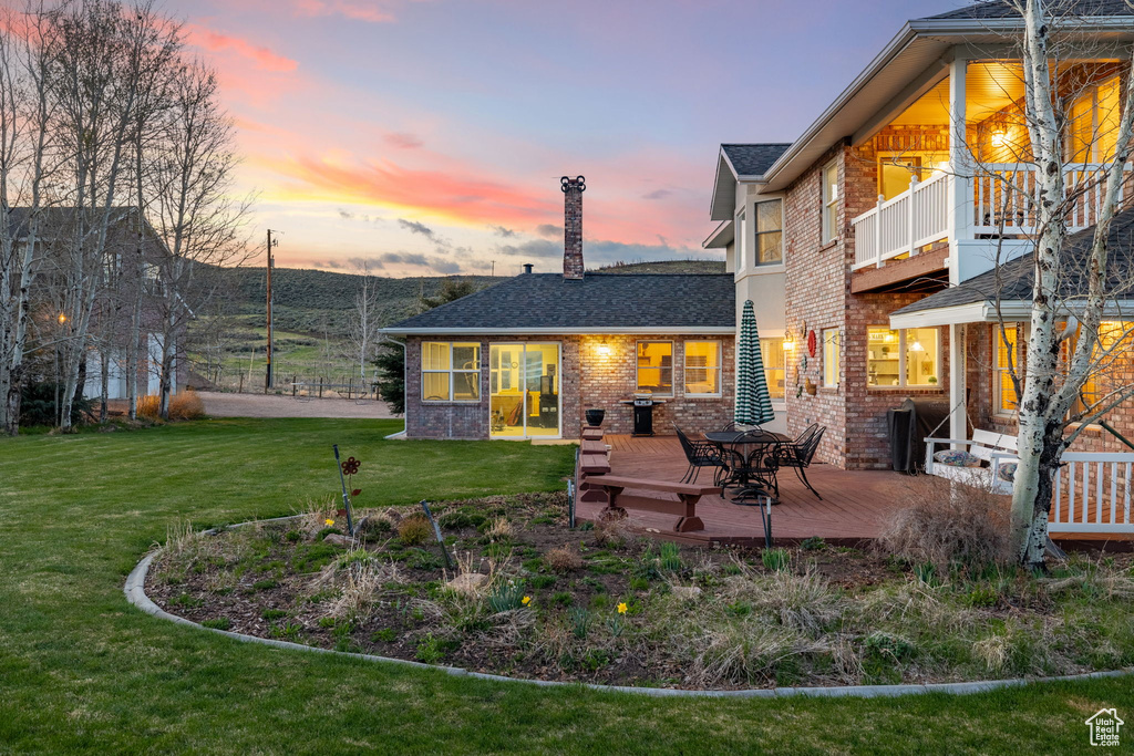 Back of property at dusk with a lawn, roof with shingles, a deck, and brick siding