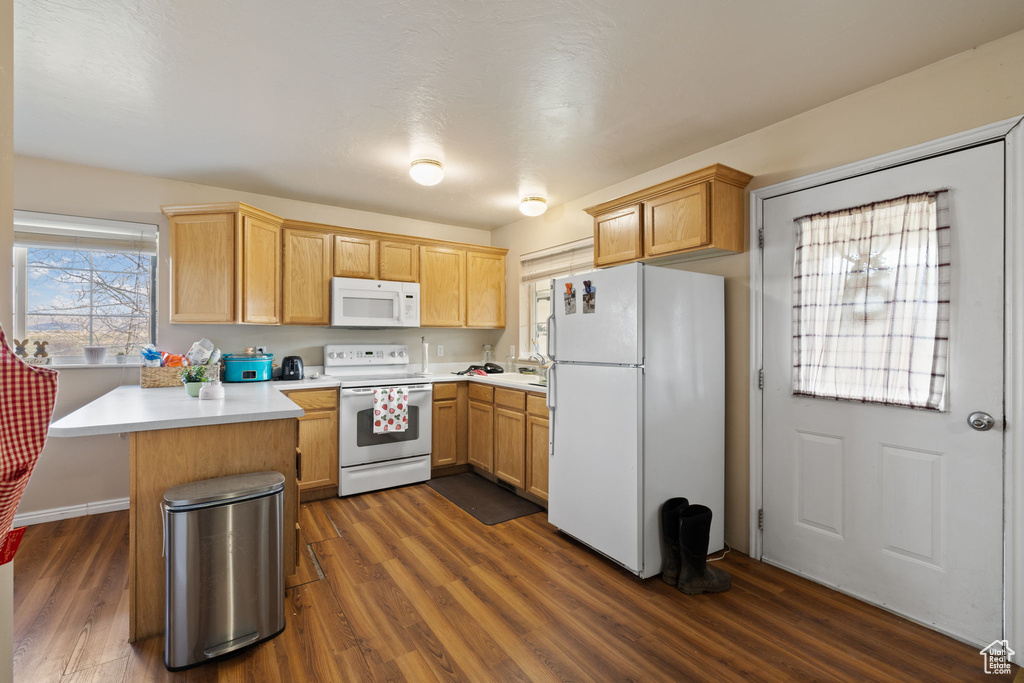 Kitchen with dark wood-style flooring, white appliances, light countertops, a peninsula, and baseboards