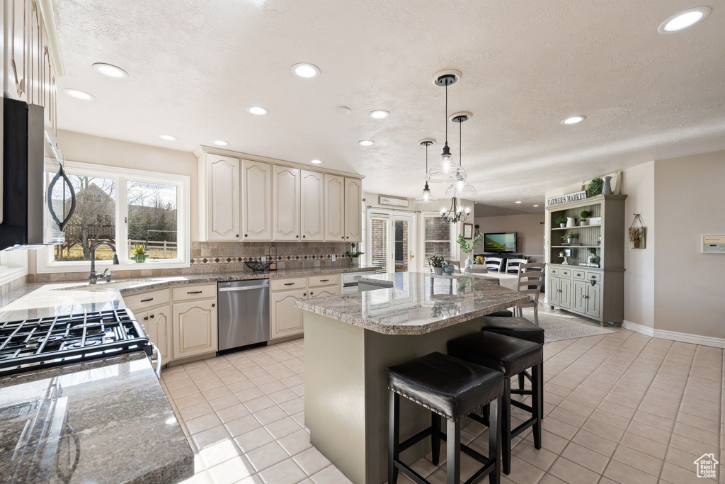 Kitchen featuring a center island, cream cabinetry, a sink, light tile patterned floors, and stainless steel appliances