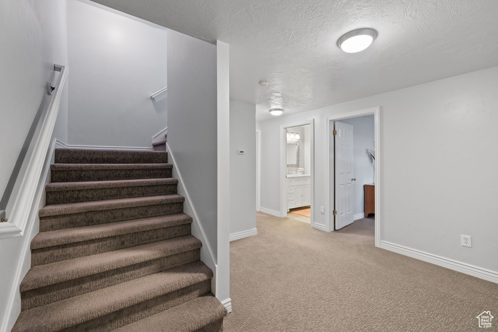 Stairway with carpet flooring, a textured ceiling, and baseboards