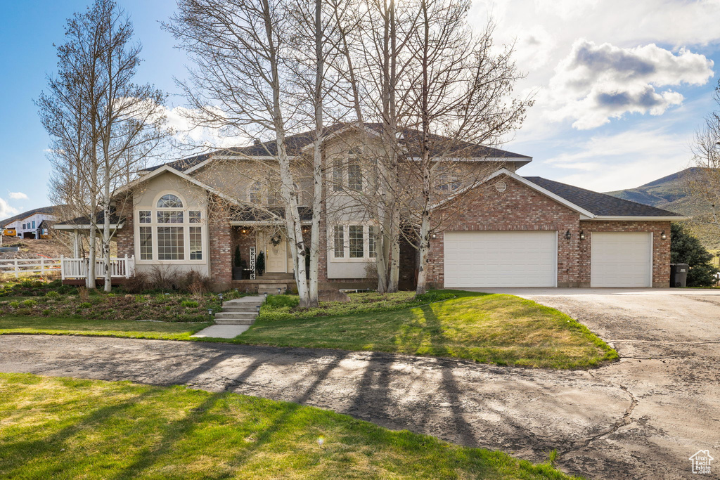 Traditional-style house with an attached garage, driveway, a front lawn, and brick siding