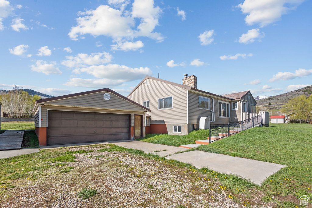 View of front of home featuring driveway, a chimney, a front yard, an outbuilding, and a garage