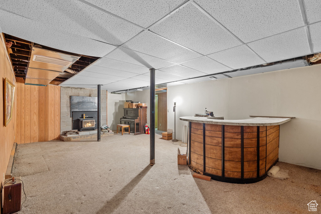 Finished below grade area featuring carpet flooring, a drop ceiling, and a wood stove