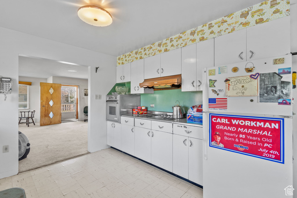 Kitchen with freestanding refrigerator, white cabinetry, light floors, under cabinet range hood, and stovetop