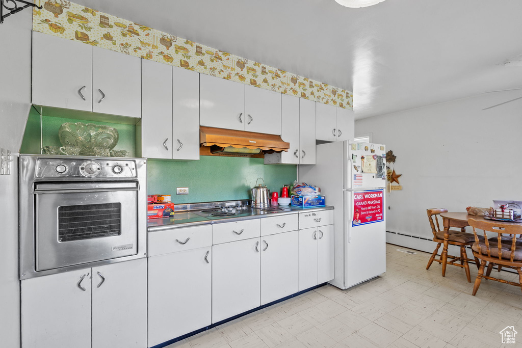 Kitchen with electric stovetop, freestanding refrigerator, light floors, under cabinet range hood, and oven