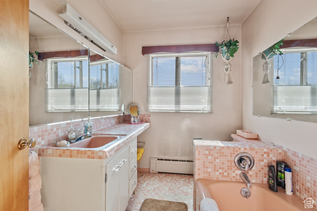 Full bath featuring decorative backsplash, a baseboard heating unit, a bath, and a wealth of natural light