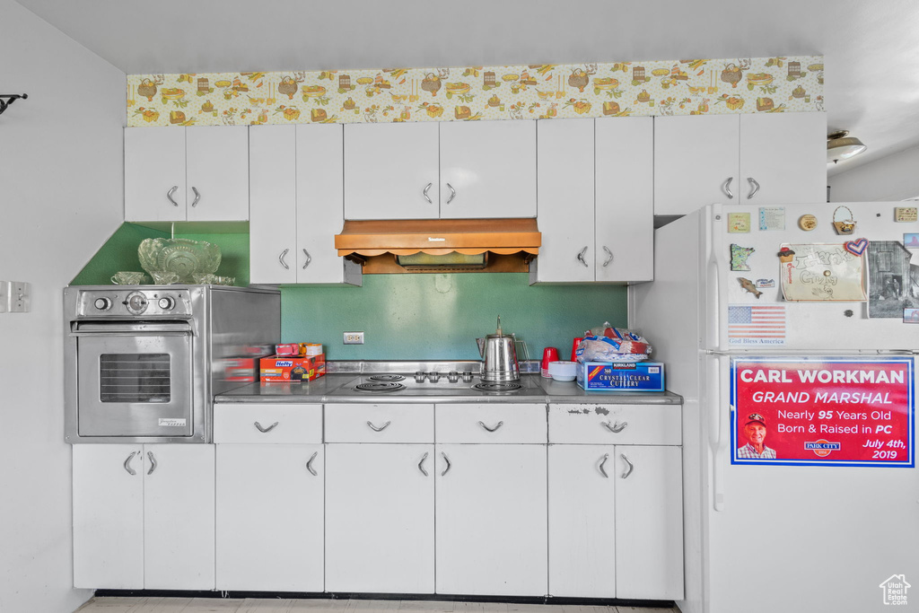 Kitchen featuring white cabinets, freestanding refrigerator, under cabinet range hood, and oven
