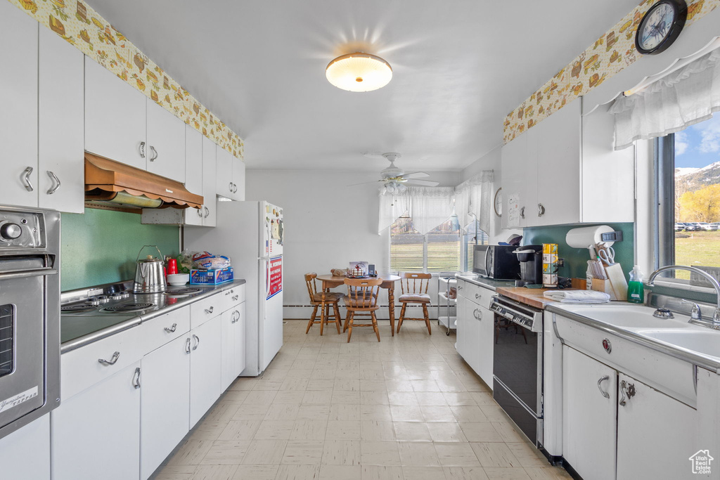 Kitchen with light countertops, white cabinetry, a baseboard heating unit, under cabinet range hood, and stainless steel appliances