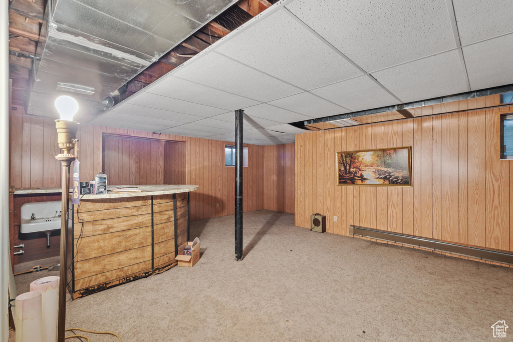 Finished basement featuring a bar, wood walls, carpet, and a drop ceiling